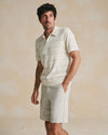 Man wearing a light-colored polo shirt and shorts against a beige background