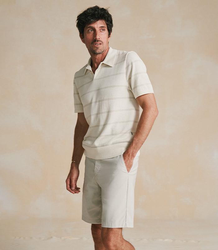 Man wearing a light-colored polo shirt and shorts against a beige background