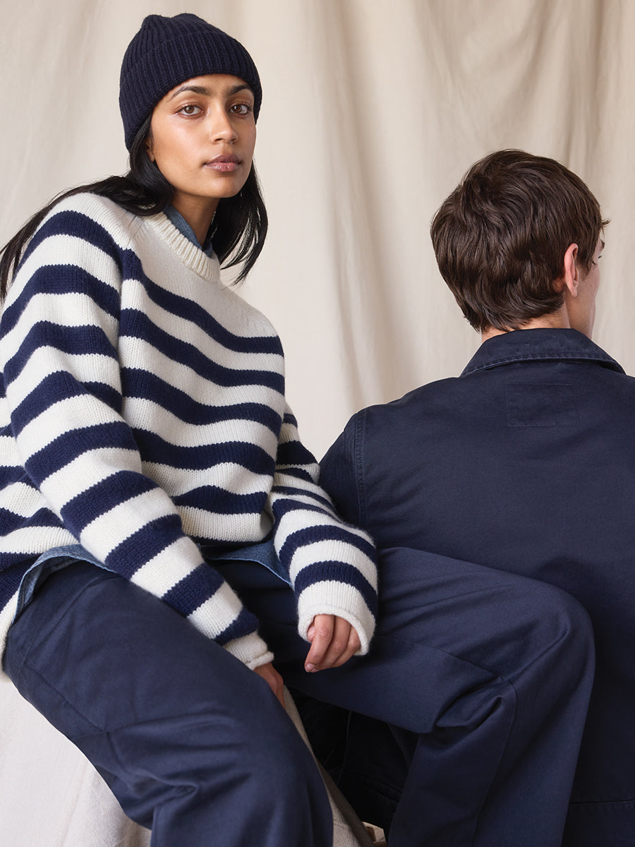 Two people sitting on a white couch, one wearing a navy and white striped sweater and beanie, the other in a navy jacket.